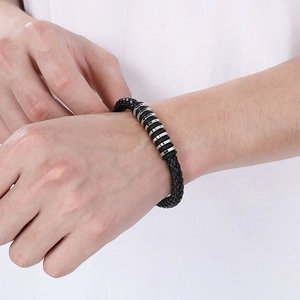 Close-up of a men's woven black leather bracelet with stainless steel rings on a wrist