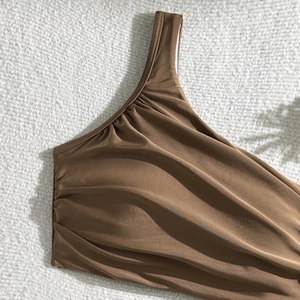 Detail of ruched dark brown one-shoulder bikini top with elegant satin finish on plush fabric