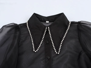 Detail of elegant black sheer organza shirt with white pearl trim on the pointed collar