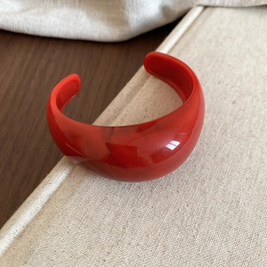 Close-up of a vibrant red resin cuff bracelet with marbled texture on fabric background