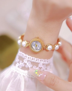 Detailed view of luxury gold quartz watch with pearl bracelet strap on female wrist