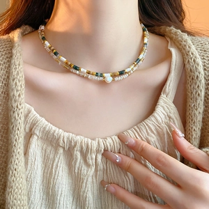 Detail of layered gold-plated necklace featuring heart-shaped pearl and colorful beads