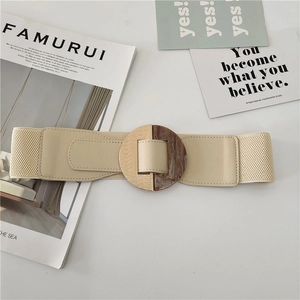 Detail of beige elastic waist belt featuring a round gold and marble textured buckle