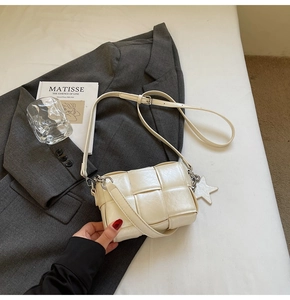 Détail du sac bandoulière tressé blanc crème avec breloque étoile sur blazer gris