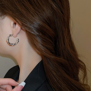Close-up of silver C-shaped lava earrings with irregular liquid metal texture on ear