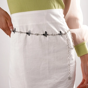 Détail d'une ceinture chaîne argentée avec papillons noirs sur jupe blanche