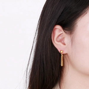 Detail view of gold stainless steel Cuban chain tassel earrings on model