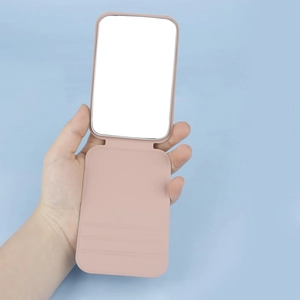Detailed close-up of a pink portable folding makeup mirror held by hand for scale