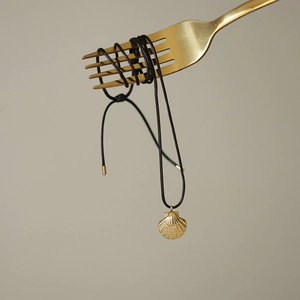 Minimalist black rope necklace with golden shell pendant on a golden fork display