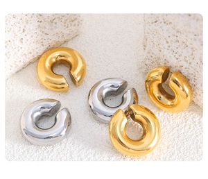 Detail view of gold and silver polished C-shaped ear cuffs on white textured stone