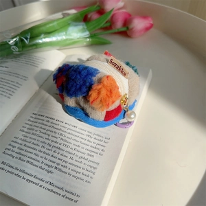 Dettaglio della pochette in peluche con pompon colorati e cerniera con perla