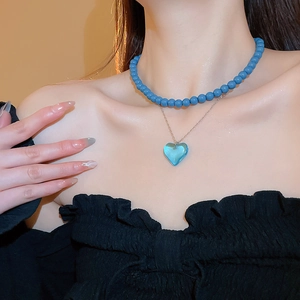 Detail of double-layer heart pendant necklace with blue beads on a female model