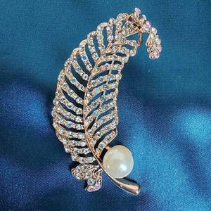 Elegant rose gold feather brooch with white rhinestones and a large pearl on blue satin