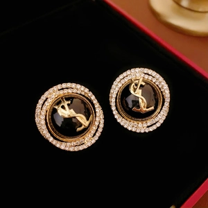 Macro detail of luxury gold-tone monogram earrings with black core and crystal pavé rim