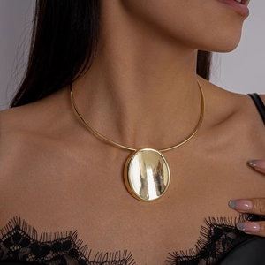 Detail eines hochglanzpolierten goldenen ovalen Anhängers an einem starren Choker-Halsreif