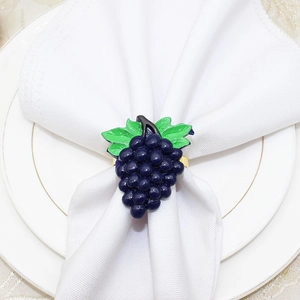 Detail of purple grape napkin ring with green leaves on golden base over white cloth