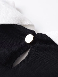 Detail shot of black knitted polo top with white lapel collar and gold button accent