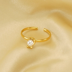 Adjustable golden stainless steel open ring with single pearl on a luxury satin background
