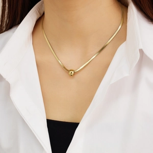 Detail of a gold flat snake chain necklace with a faceted geometric ball pendant on a model