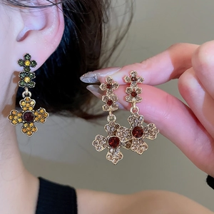 Close-up of vintage floral cross earrings with red and green gemstones in gold finish