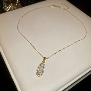 Macro view of gold teardrop pendant featuring pavé zircons and triple white pearls