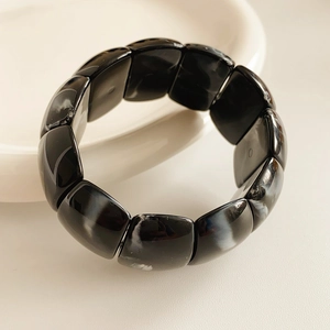 Detail of black marble acrylic stretch bracelet on a white porcelain plate