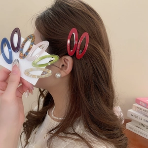 Detail showing various colorful oval acetate hair clips on a card and worn by a model