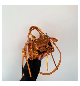 Close-up of metallic orange patent leather handbag with silver studs and heart mirror