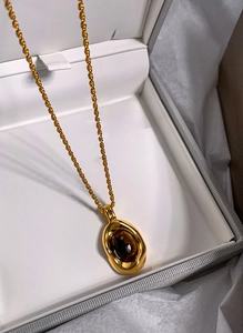 Close-up of golden oval tiger eye pendant on a delicate gold twisted chain necklace