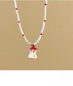 Detail of red and white beaded necklace featuring a unique bitten apple core resin pendant