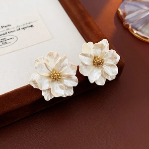 Close-up of pearl white resin flower earrings with golden center and radial texture