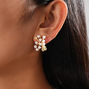 Close-up of elegant gold earring with pearl flower cluster and leaf detail on model