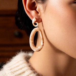 Detail view of large acrylic oval drop earrings with amber marble pattern on a model