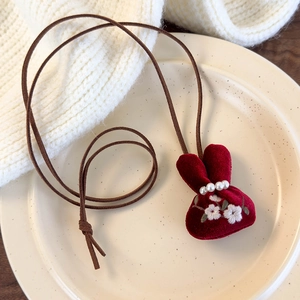 Detail of red velvet lucky bag pendant with white embroidery and pearls on brown cord
