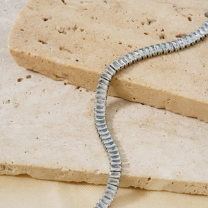Elegant silver square cut zircon necklace draped over travertine and champagne silk fabric