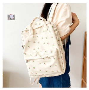 Side view of floral backpack with pink blossoms, front pocket and top handle detail