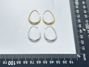 Close-up of gold and silver U-shaped drop earrings with measurement scale detail