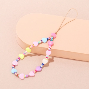 Macro shot of colorful clay evil eye phone charms with heart beads on pink textured surface