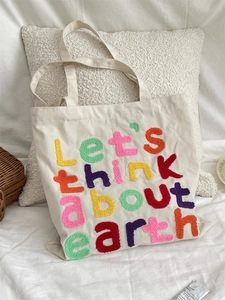 Detail of colorful chenille embroidery on cream canvas tote bag with eco slogan