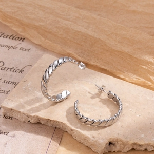 Silver twisted rope C-shaped stainless steel hoop earrings on a textured stone surface