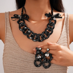 Detail of acrylic chain necklace with black bow, splash ink texture, and pearl earrings