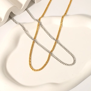 Detailed view of silver and gold stainless steel curb chains on a white tray