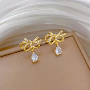 Detailed macro view of golden bow earrings with sparkling zircon and teardrop crystals