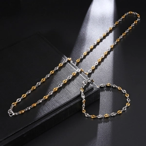 Detailed close-up of two-tone coffee bean link necklace and bracelet set on a black box