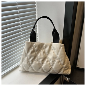 Detail of white quilted tote bag with wide black straps in a soft lighting scene