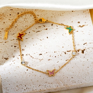 Elegant gold butterfly bracelet with colorful enamel charms on a beige stone