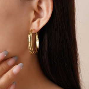 Close-up of golden geometric double hoop earrings with textured diamond-cut details on model