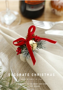 Detail of Christmas napkin ring with red velvet bow, pine cone, and gold bell decoration