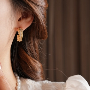 Close-up of 18k gold plated C-shaped earrings with fine crystals worn by a model