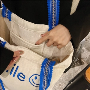 Detail view of the canvas tote bag showing the interior open pocket and blue smile embroidery